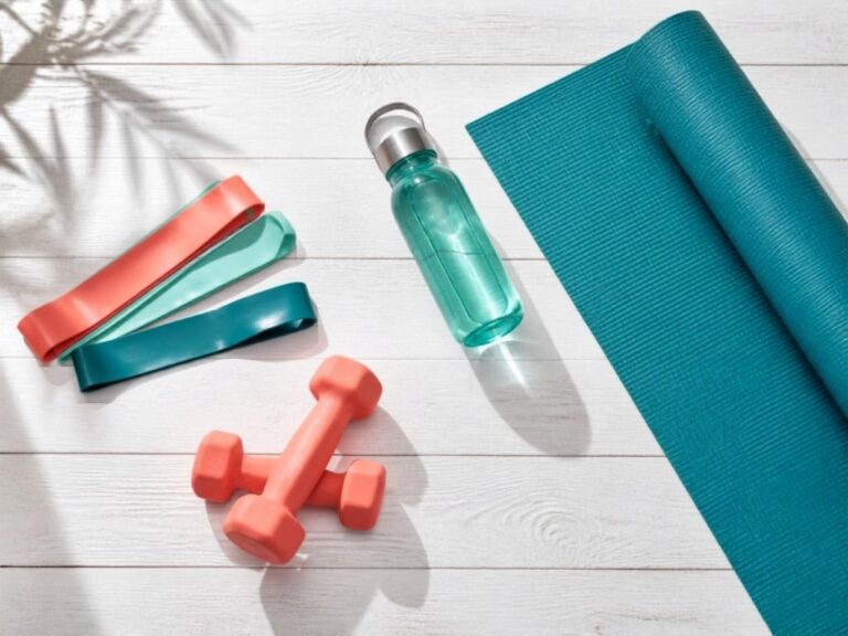 Yoga mat, resistance bands, dumbbells and water bottle on white wooden floor for belly fat workout at home
